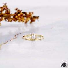 a yellow gold ring with a single diamond on the surface next to some dried flowers