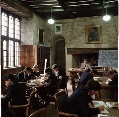 a group of people sitting at desks in a room with windows and pictures on the wall