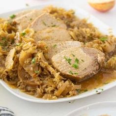 a white plate topped with meat and gravy next to an apple slice on top of a table