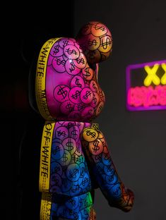 a multicolored teddy bear is standing in front of a neon sign that says xx