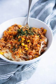 a white bowl filled with food on top of a blue and white table cloth next to a fork