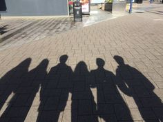 the shadow of three people standing next to each other on a brick walkway in front of a building