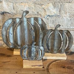 three metal pumpkins sitting on top of a wooden stand next to a brick wall