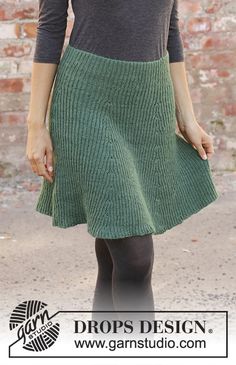 a woman standing in front of a brick wall wearing a green skirt and black tights