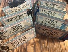 some frozen princess signs are sitting on a wooden table with snowflakes and other decorations