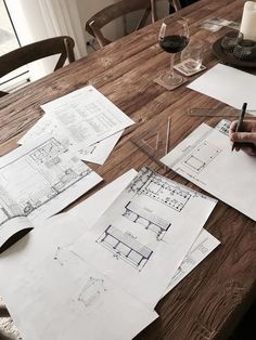 a table with drawings and wine glasses on top of it next to a person's hand holding a pen