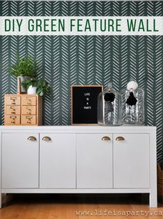 the diy green feature wall is next to a white cabinet with two vases on top