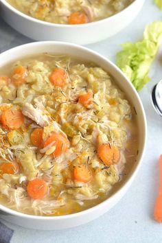 two bowls of chicken and vegetable soup on a table with carrots, celery, and parsley