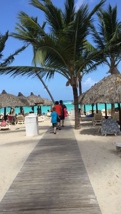 people walking on the beach with umbrellas and palm trees