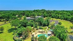 an aerial view of a large home surrounded by trees and green grass with a swimming pool in the middle