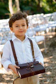 a young boy wearing suspenders and holding a brown briefcase in front of white tables