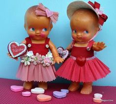 two little dolls standing next to each other on a table with heart shaped candies