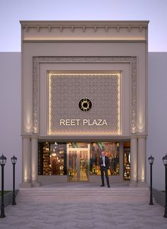 a man standing in front of a store with lights on it's windows and the words reef plaza lit up at night