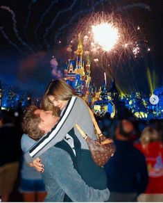 a man and woman kissing in front of the disney castle at night with fireworks behind them