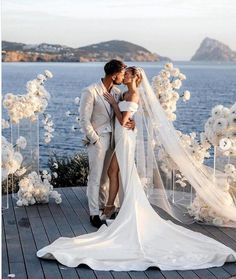 a bride and groom standing on a dock with white flowers