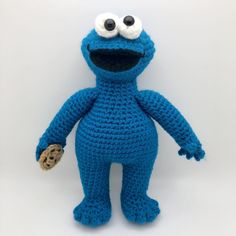 a crocheted blue stuffed animal with big eyes and a cookie in his hand