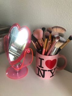 a pink mug with makeup brushes in it sitting on a table next to a mirror