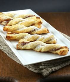 several pastries on a white plate sitting on a wooden table next to a cloth