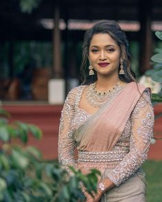 a woman in a pink and beige outfit standing next to a tree with her hands on her hips