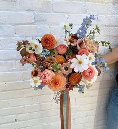 a woman standing next to a brick wall holding a bouquet of flowers