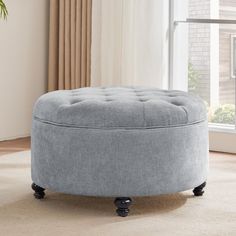 a grey round ottoman sitting on top of a carpeted floor next to a window