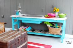 a blue table sitting next to a sink on top of a wooden box filled with flowers