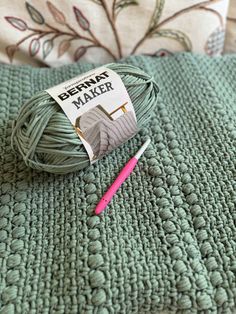 a ball of yarn sitting on top of a bed next to a crochet hook