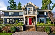 a blue house with red door and steps leading up to the front entrance, surrounded by greenery