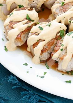 meat covered in gravy on a white plate with sauce drizzled over it