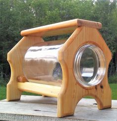 a wooden bench with a large glass jar on it's back end, sitting in front of some trees