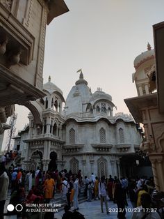 many people are walking around in front of a white building with arches and pillars on the sides