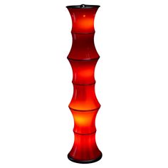 a tall red glass vase sitting on top of a white table next to a lamp