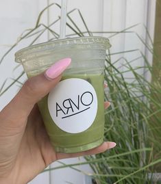 a hand holding a green cup with the word ovra on it and a pink manicure