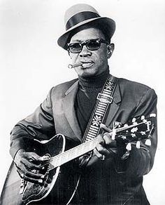 a man in a suit and hat playing an acoustic guitar