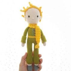 a hand holding a crocheted doll in front of a white background