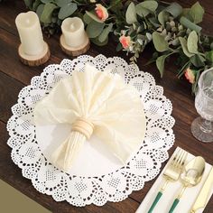 a place setting on a wooden table with white lace doily and flowers in the background