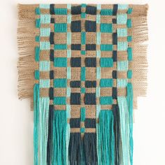 a woven wall hanging with tassels on the bottom and green, black and tan colors