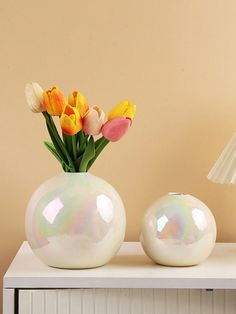 there are two vases with flowers in them on the table next to a lamp