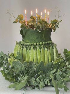 a green cake with candles on top of it surrounded by leaves and ivy, sitting on a white table cloth