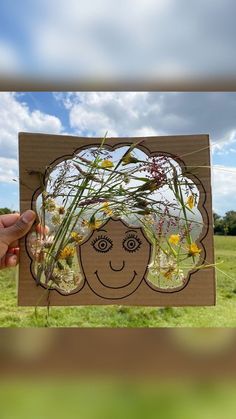 a person holding up a cutout with flowers and grass in front of the image