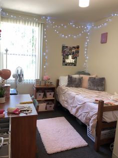 a bedroom with a bed, desk and window in the corner is lit up by fairy lights