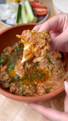 a hand holding up a piece of food over a bowl filled with vegetables and sauce