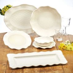 a table topped with white dishes and plates on top of a wooden table next to flowers