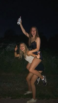 two young women posing for the camera at night, one holding a bottle and the other standing up