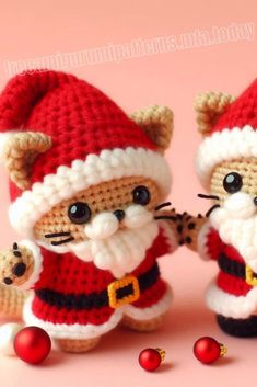 two small crocheted cats dressed up as santa clause and holding hands with christmas balls