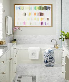 a bathroom with white cabinets and marble counter tops, an art piece on the wall above the bathtub