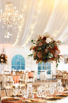 a tall vase filled with flowers sitting on top of a table covered in white linens