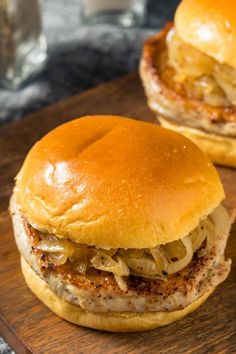 two hamburgers sitting on top of a wooden cutting board