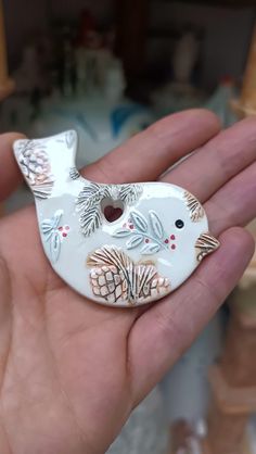 a hand holding a white ceramic bird ornament with leaves and acorns