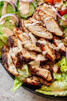 a salad with chicken, lettuce, cucumber and tomatoes on it